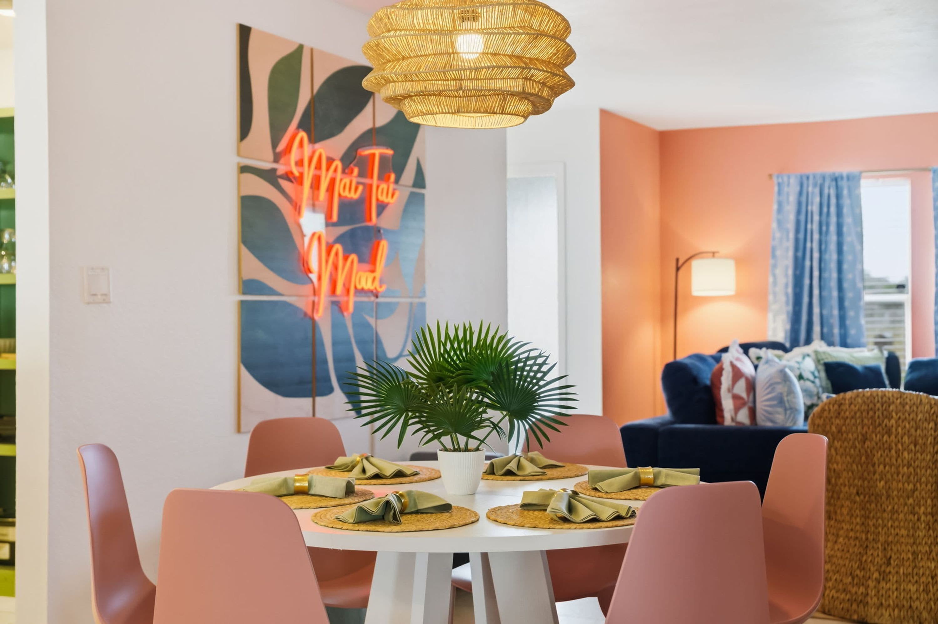 Un comedor con una mesa redonda, sillas, una lámpara colgante y una pared con un letrero de neón.