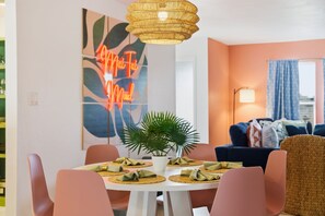 A dining area with a round table, chairs, a hanging light fixture, and a wall with a neon sign. - Epic Backyard - Private Pool - Firepit - Putt Putt (Seminole)