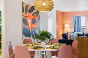 Un comedor con una mesa redonda, sillas, una lámpara colgante y una pared con un letrero de neón.