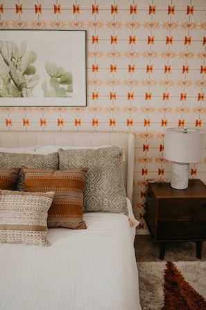 A bedroom with a bed, pillows, a nightstand, a lamp, and a wall with a geometric pattern. - Casa de Oro Saguaro Views Pool Hot Tub (Tucson)