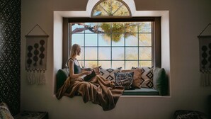 A person sitting on a cushioned bench by a large window with a view of trees and sky. - Casa de Oro Saguaro Views Pool Hot Tub (Tucson)