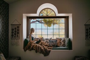 A person sitting on a cushioned bench by a large window with a view of trees and sky. - Casa de Oro Saguaro Views Pool Hot Tub (Tucson)