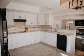 A modern kitchen with white cabinetry, a black dishwasher, and a tiled backsplash. - Casa de Oro Saguaro Views Pool Hot Tub (Tucson)