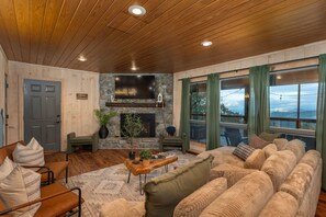 Uma sala de estar aconchegante com lareira de pedra, teto de madeira e grandes janelas.