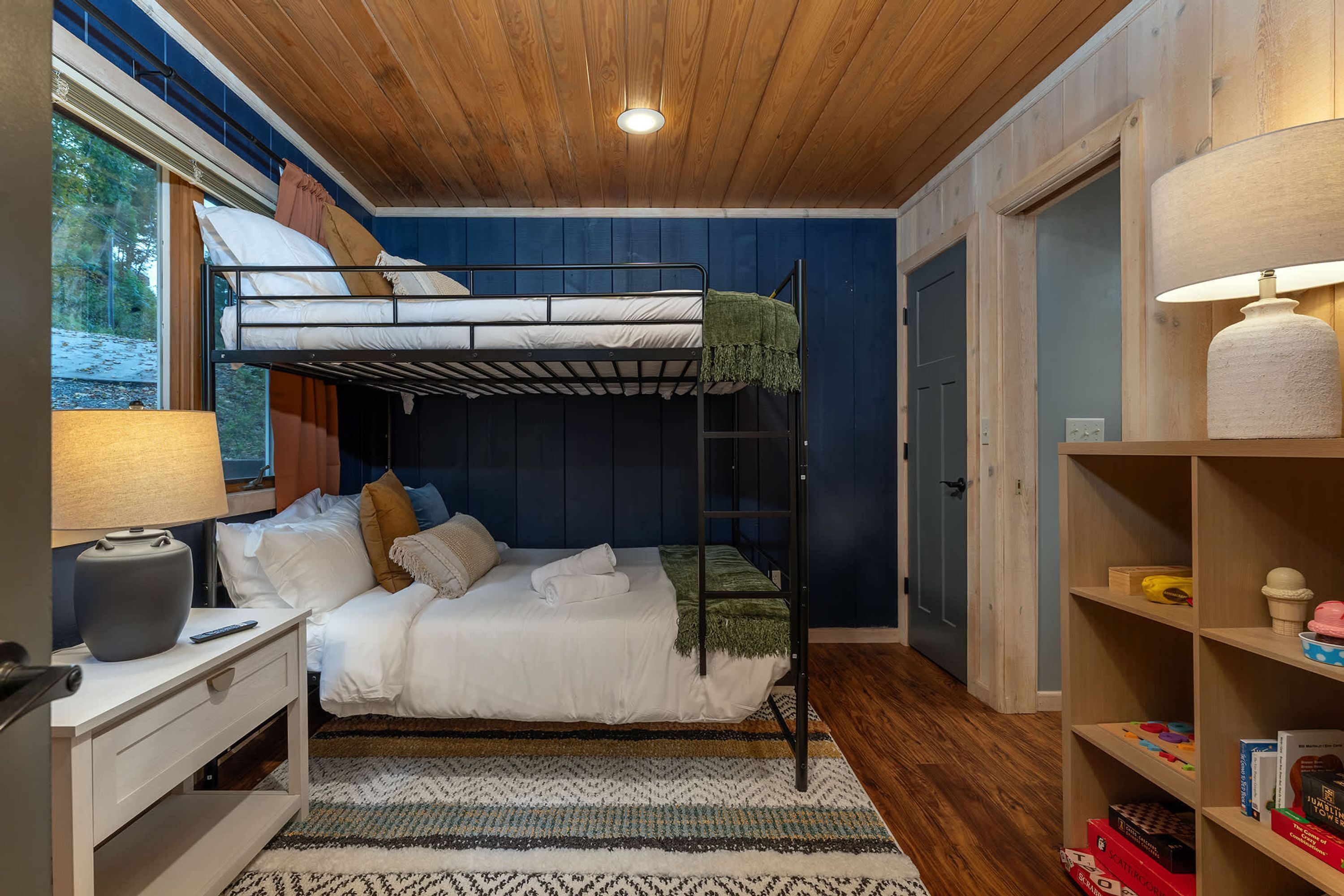 A bunk bed room with a desk, a lamp, and a bookshelf.
