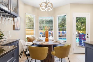 A dining area with a round table, two chairs, a chandelier, and a view of a pool through large windows. - Resort Style Backyard Arcade Games Hot Tub (San Antonio)