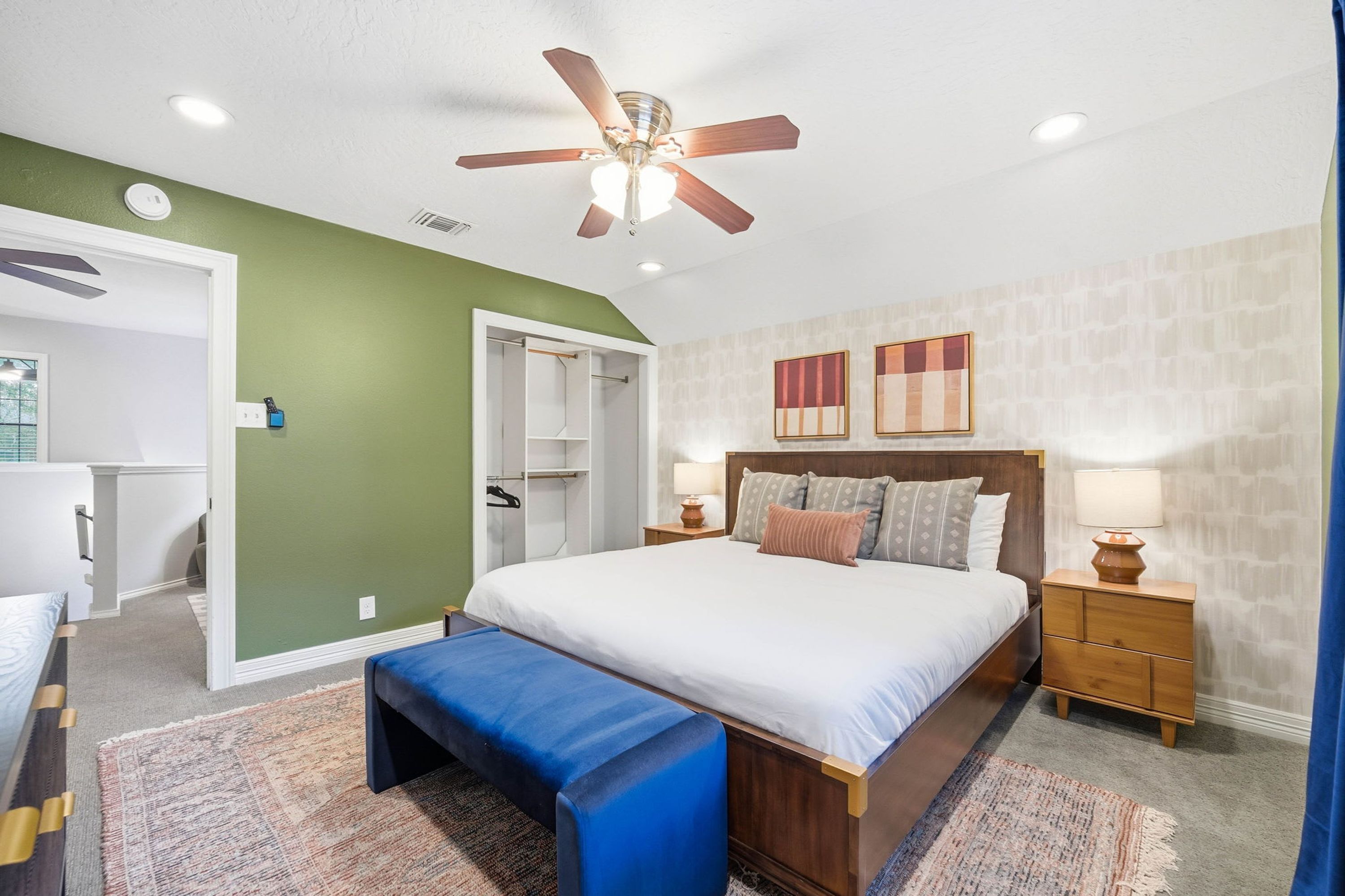 A bedroom with a bed, bedside tables, a bench, a ceiling fan, and a walk-in closet.