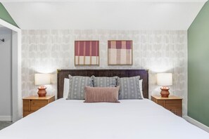 Ein Hotelzimmer mit einem großen Bett, zwei Nachttischen, einem Holzkopfteil und zwei an der Wand befestigten Kunstwerken.