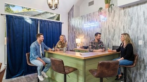 Un groupe de quatre personnes est assis autour d’un comptoir en bois, dans un espace bar agrémenté d’un rideau bleu et d’un mur au motif texturé.