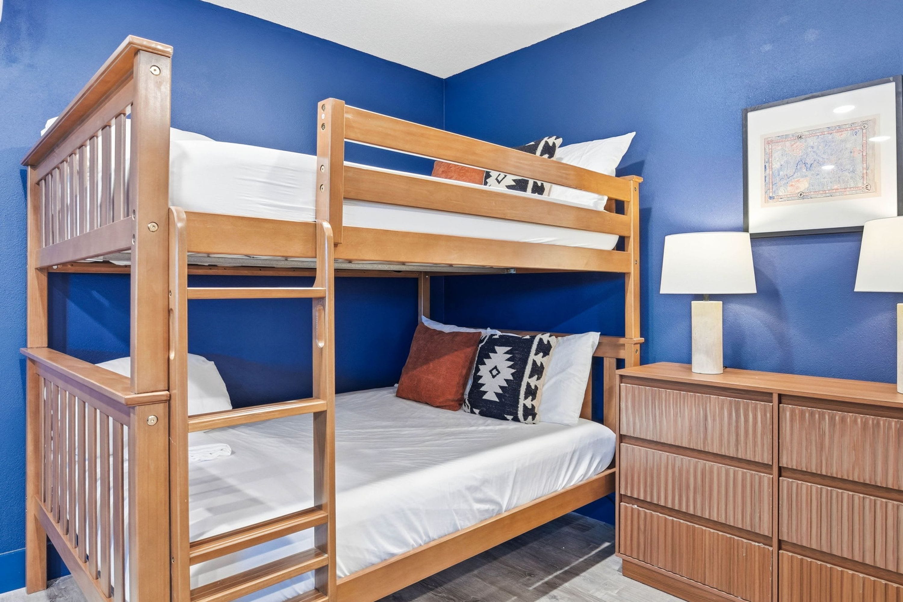 A bunk bed with a wooden frame, white bedding, and a nightstand with a lamp.