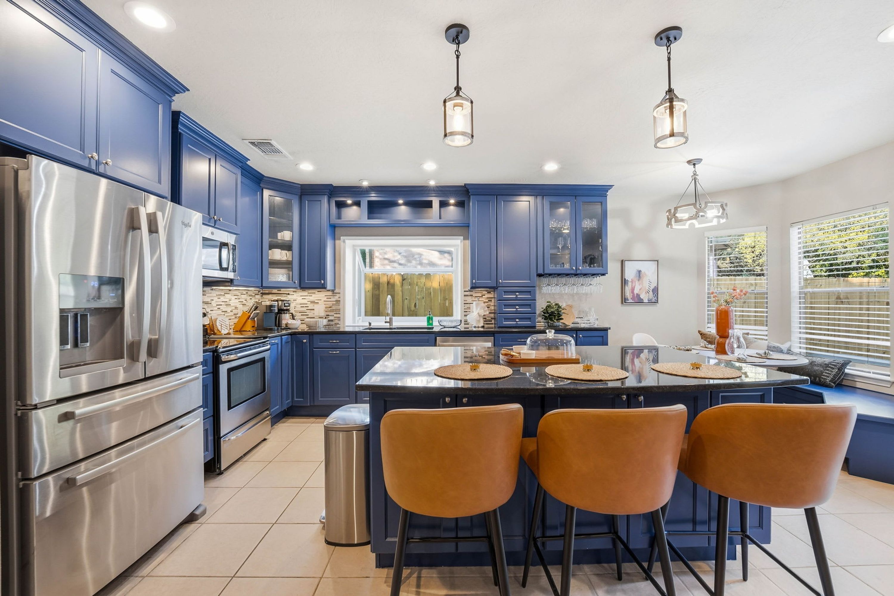 Een moderne keuken met blauwe kastjes, roestvrijstalen apparatuur en een centraal eiland met stoelen.
