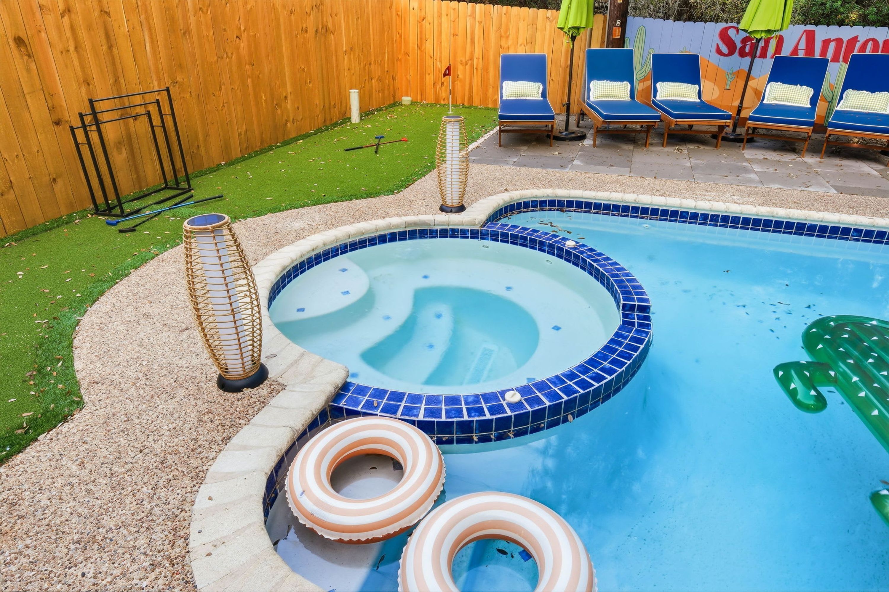Een zwembad met een hottub, omringd door een houten hek, en een cactussenmuur op de achtergrond.