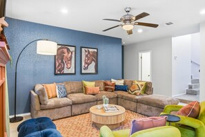 Ein Wohnzimmer mit einem Ecksofa, bunten Kissen, einem Couchtisch und einem Deckenventilator.