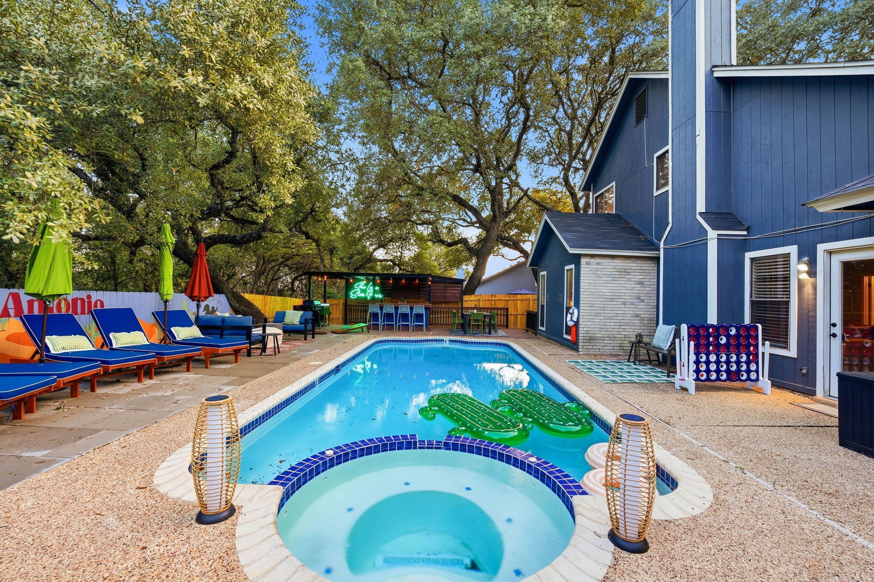 A swimming pool with lounge chairs and a hot tub, surrounded by trees and a building.