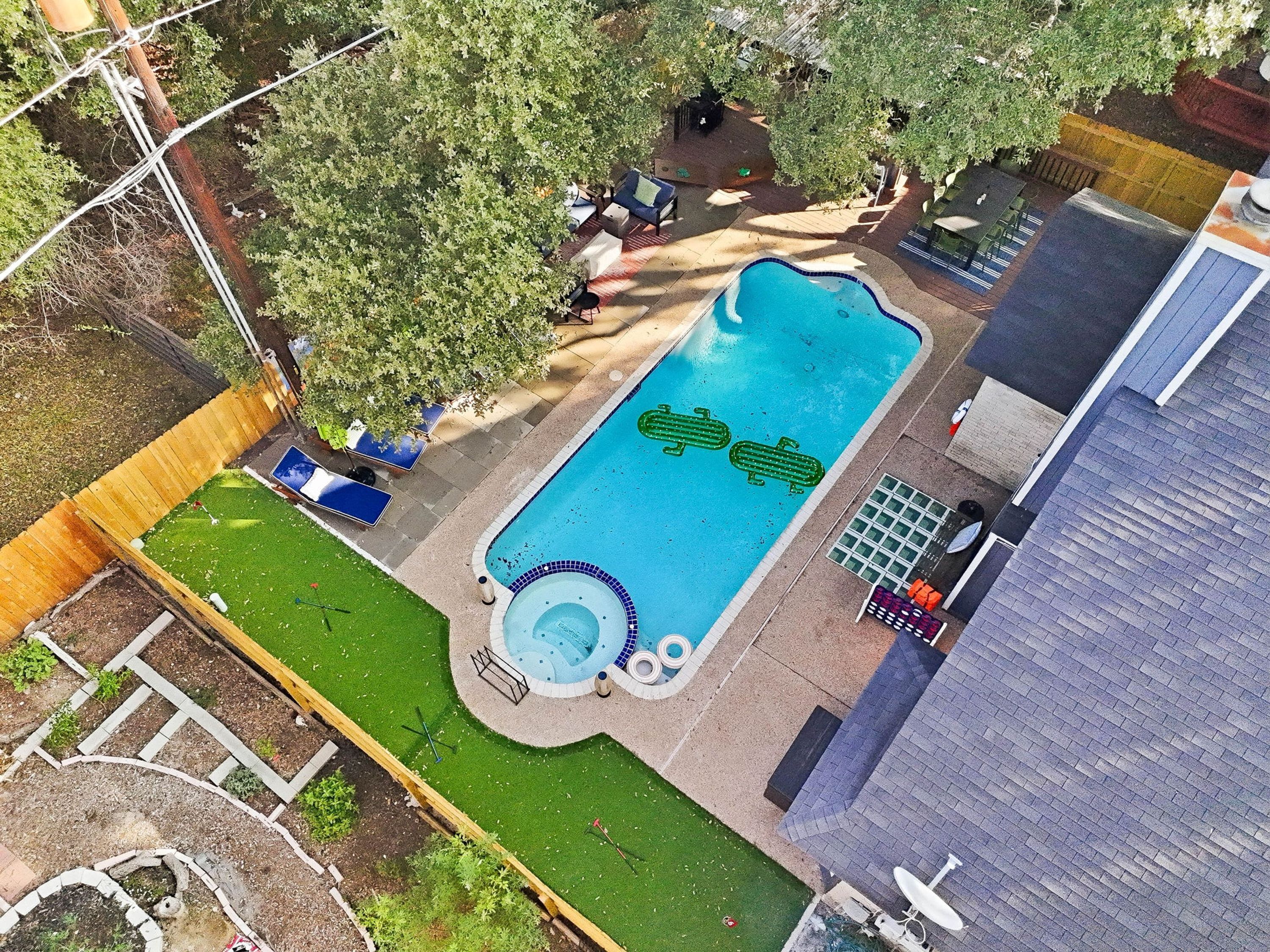 Vista aérea de un patio trasero con piscina, un jacuzzi y un área de jardín cercada.