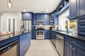 A modern kitchen with blue cabinets, stainless steel appliances, and a large window. - Resort Style Backyard Arcade Games Hot Tub (San Antonio)