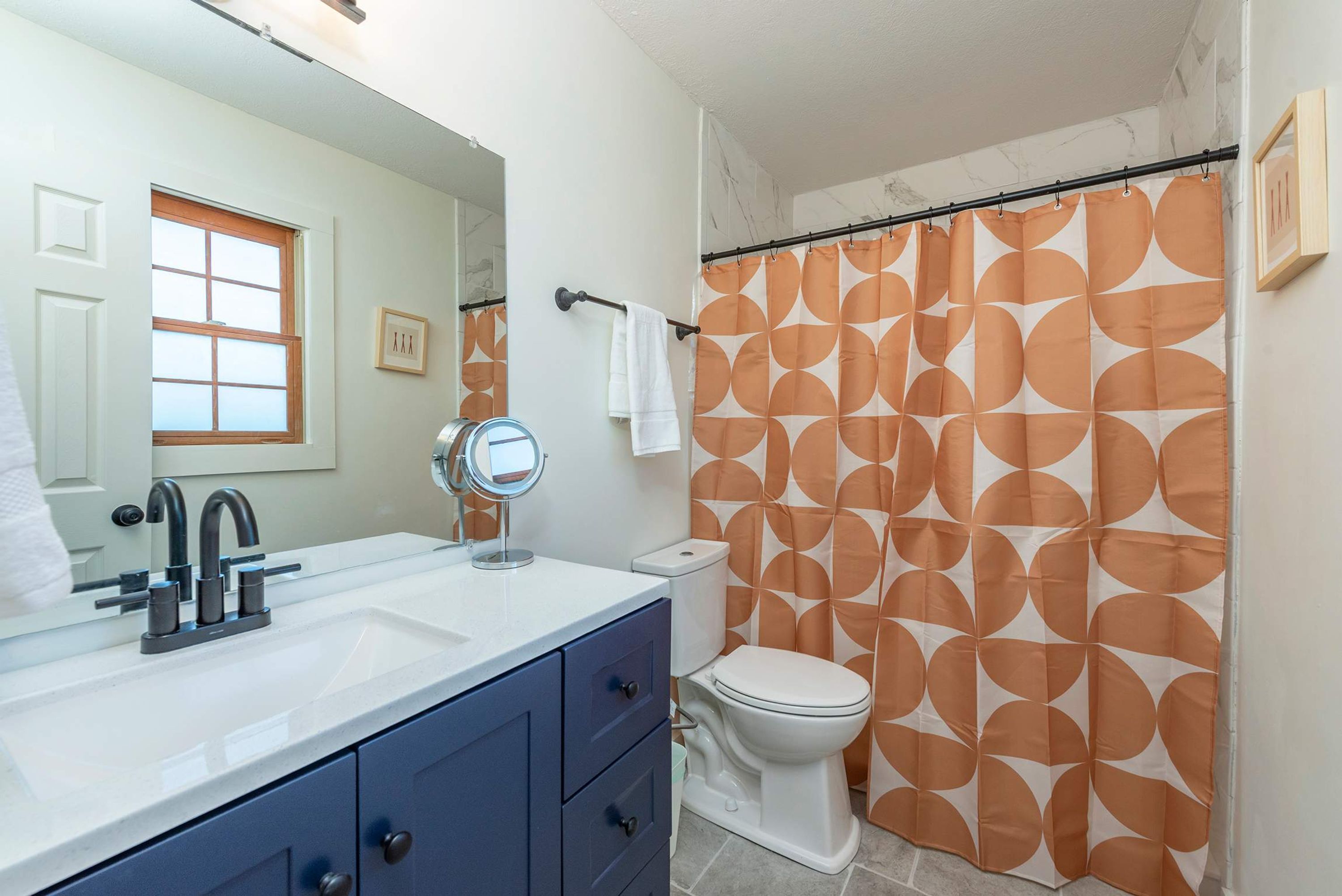 A bathroom with a white sink, a mirror, a toilet, and a shower curtain with a geometric pattern.