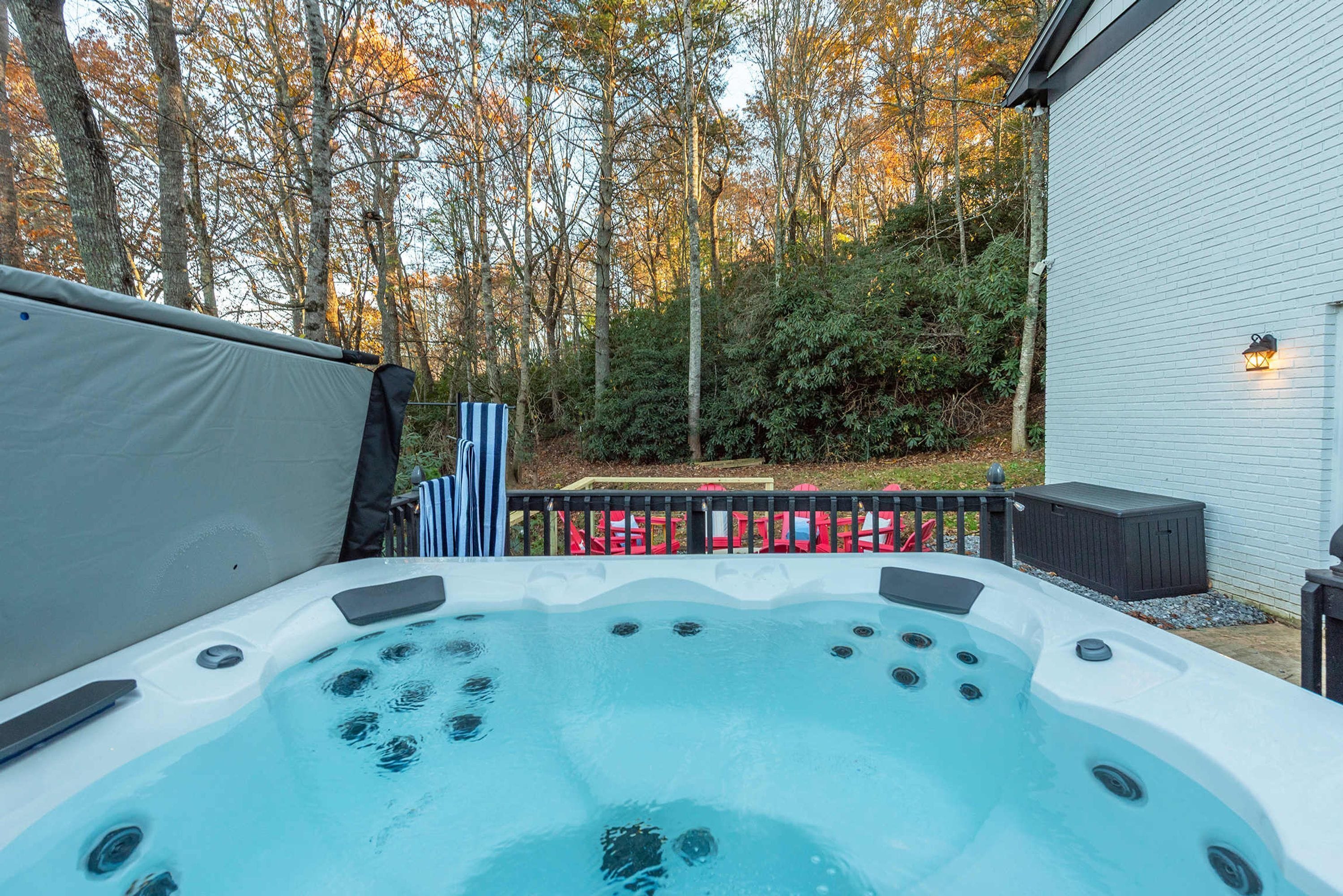 A hot tub in a backyard with a wooden deck, surrounded by trees and a white building.