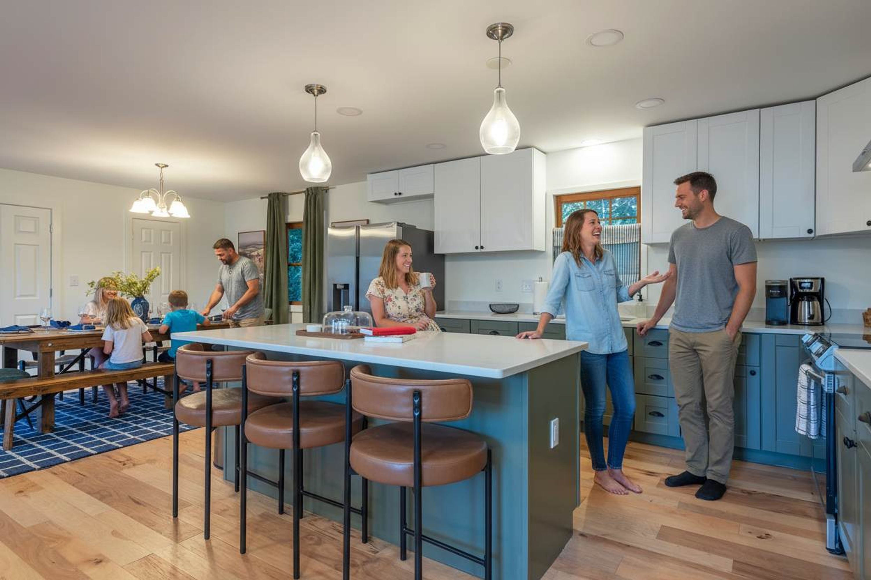 A modern kitchen with a central island, bar stools, and a dining area with a blue rug.
