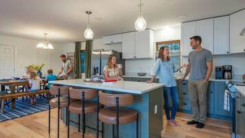 A modern kitchen with a central island, bar stools, and a dining area with a blue rug.
