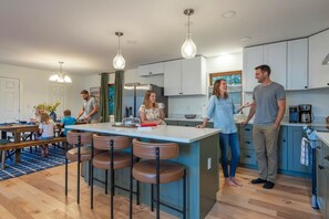 Een moderne keuken met een centraal eiland, barkrukken en een eethoek met een blauw vloerkleed.