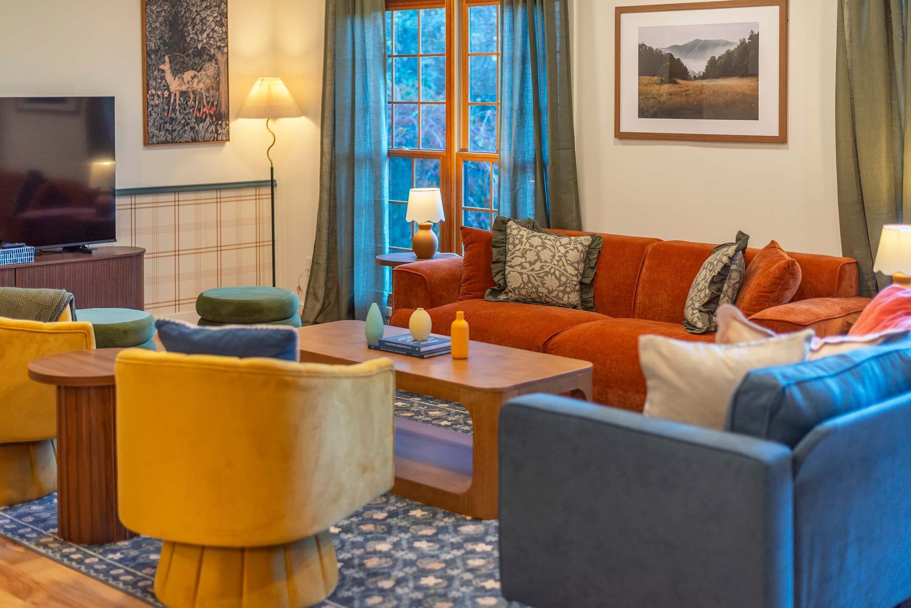 Ein Wohnzimmer mit einer Couch, Sesseln, einem Couchtisch, einem Fernseher und Kunstwerken an den Wänden.