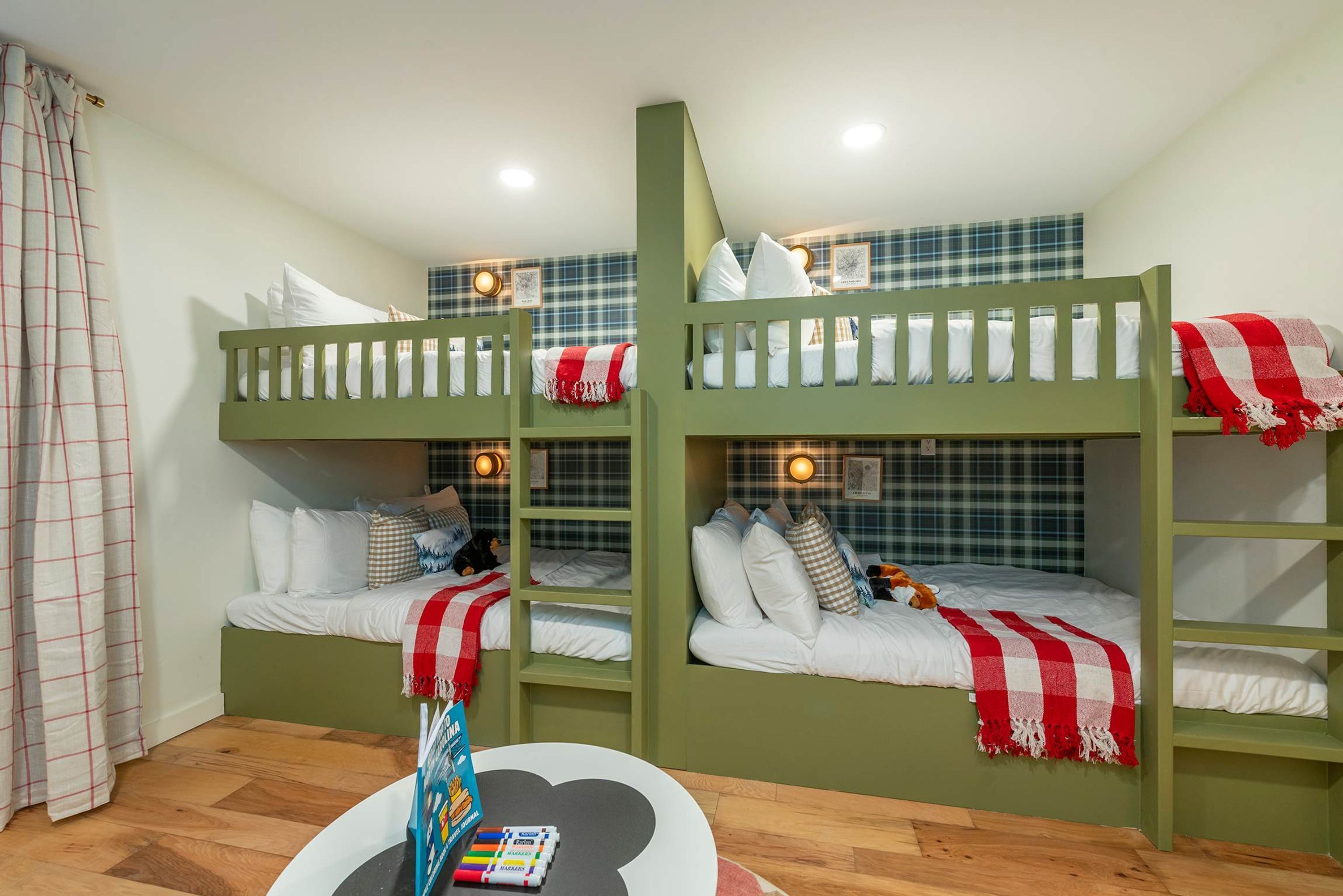 A room with bunk beds, a small table with a book, and a wall with a checkered pattern.