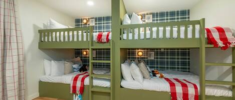 A room with bunk beds, a small table with a book, and a wall with a checkered pattern.