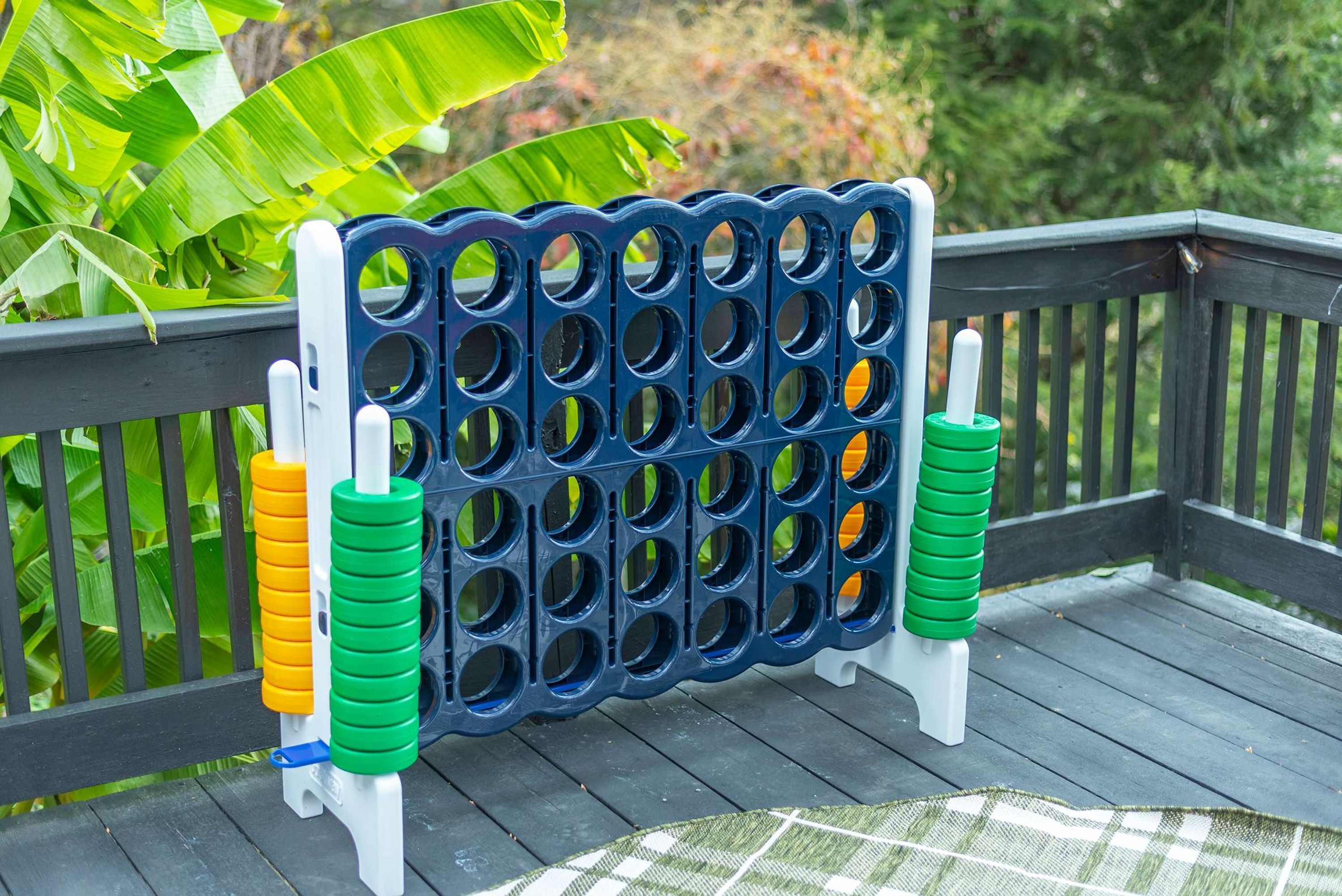 Un jeu de société est installé sur une terrasse en bois dotée d’une rambarde, le tout étant entouré de verdure.