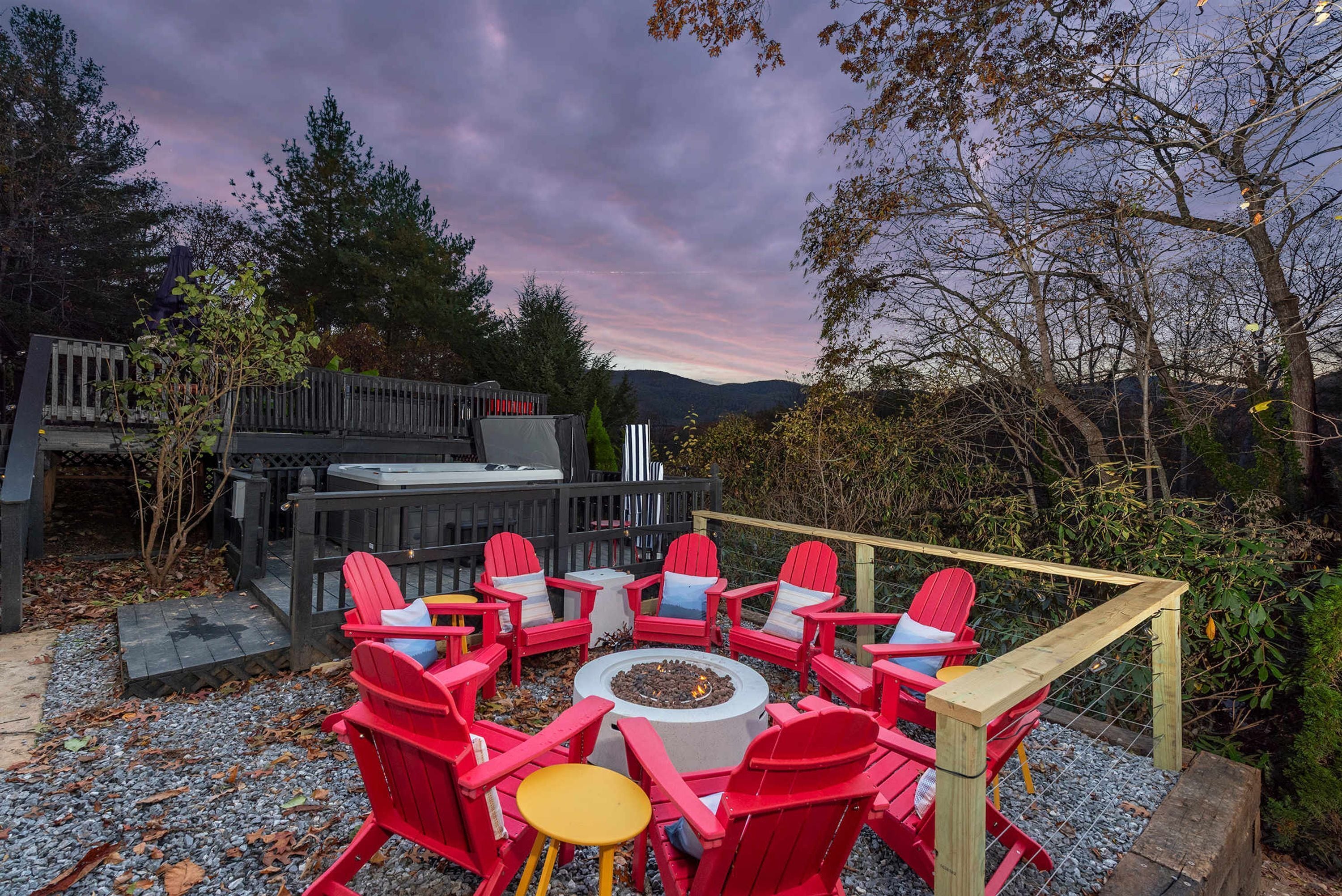 A circular seating arrangement with red chairs and a central fire pit, surrounded by a wooden deck and a view of a mountainous landscape.