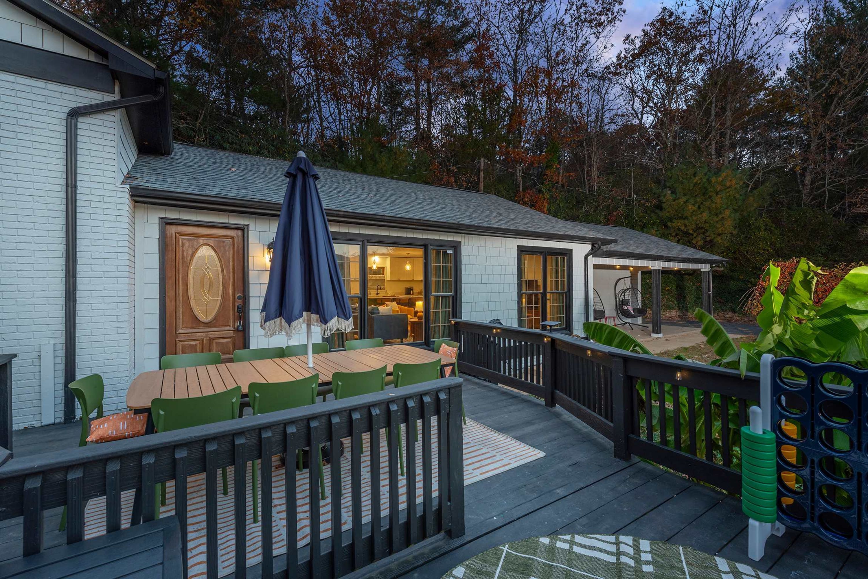 A wooden deck with a table and chairs, a covered patio area, and a view of the surrounding trees.