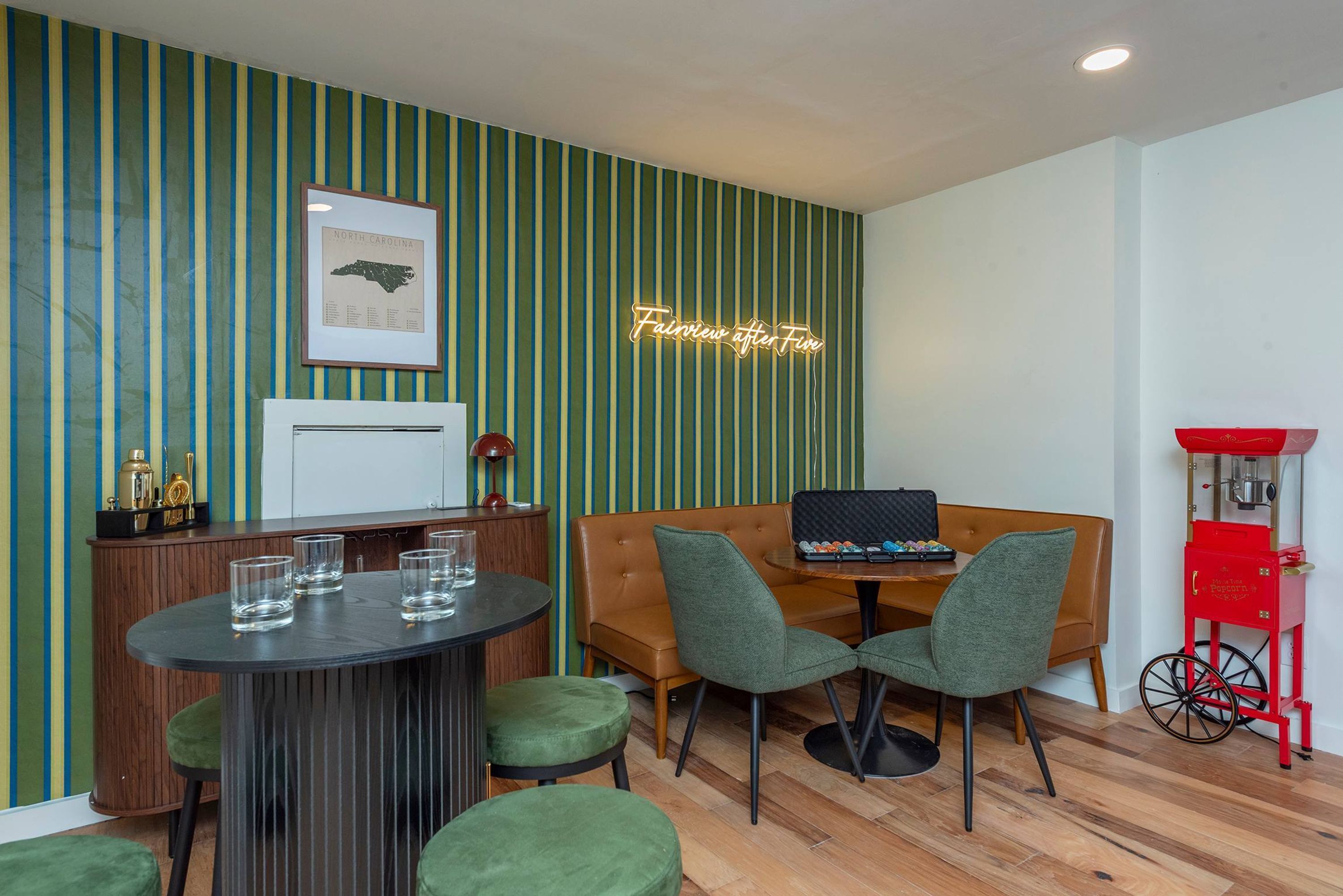 Een kamer met een gestreepte wand, een ingelijste kaart, een neonbord, een popcornmachine en een tafel met stoelen.