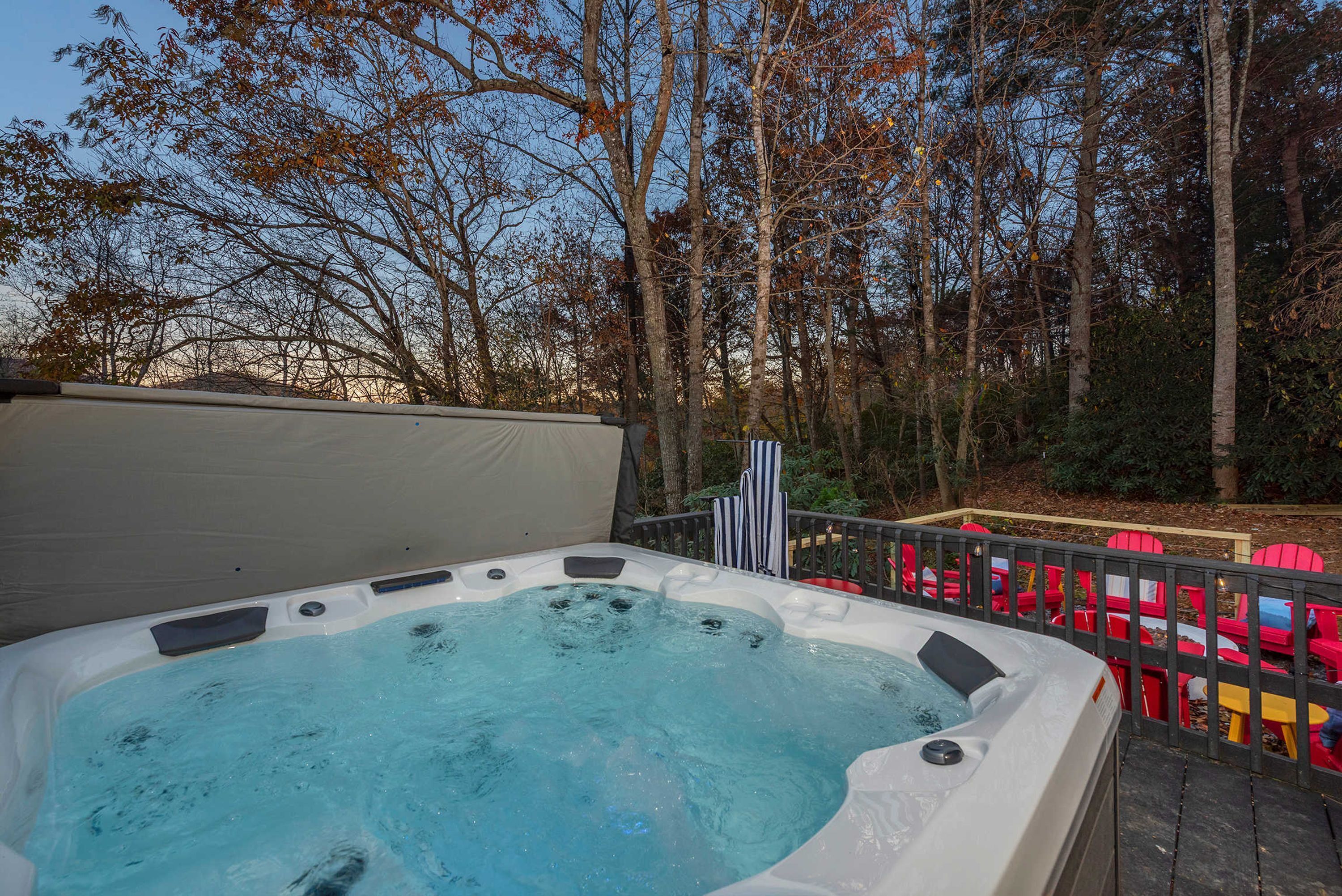 Un bain à remous avec vue sur les arbres et une terrasse en bois avec des chaises rouges.