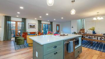 A modern kitchen with a central island, wooden flooring, and a dining area with a table and benches.