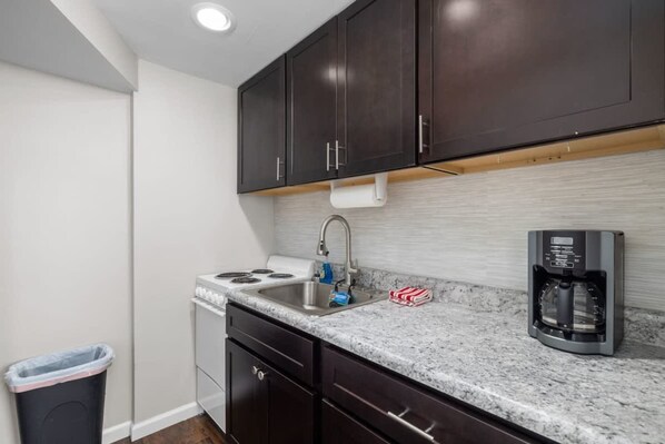 A kitchen with dark cabinets, a stainless steel sink, a stove, and a coffee maker. - Downtown Kimmswick Studio Renovated Prime Location (Imperial)