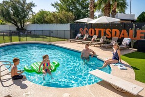 Ein Swimmingpool mit Liegestühlen und Sonnenschirmen, umgeben von einem Zaun und viel Grün.