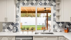 A modern kitchen with white cabinets, a stainless steel dishwasher, and a window with a view of a backyard. - The Sunkiss Pickleball Heated Pool Hot Tub (Scottsdale)