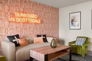 Ein modernes Wohnzimmer mit strukturierter Tapete, einer Couch mit Kissen, einem Couchtisch und einem grünen Sessel.