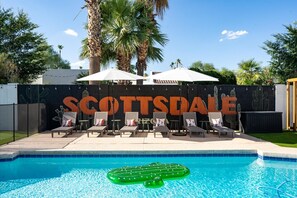 A pool area with lounge chairs and umbrellas, a sign reading 'SCOTTSDALE', and a cactus mural on the fence. - The Sunkiss Pickleball Heated Pool Hot Tub (Scottsdale)