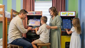A family playing arcade games, including NBA Jam and Pac-Man, in a room with bunk beds and a window. - Suncourt Retreat Sports Court Pool Hot Tub (Bradenton)