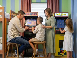 A family playing arcade games, including NBA Jam and Pac-Man, in a room with bunk beds and a window. - Suncourt Retreat Sports Court Pool Hot Tub (Bradenton)