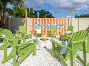 A patio area with green Adirondack chairs, a fire pit, and a decorative sign that reads 'Bradenton.' - Suncourt Retreat Sports Court Pool Hot Tub (Bradenton)