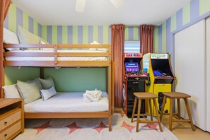 A bunk bed with pillows, a small table, and two arcade machines in a room with striped walls. - Suncourt Retreat Sports Court Pool Hot Tub (Bradenton)