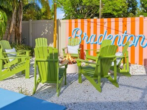 A patio area with green Adirondack chairs, a fire pit, and a decorative fence with the word 'Bradenton' on it. - Suncourt Retreat Sports Court Pool Hot Tub (Bradenton)