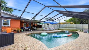 A swimming pool with lounge chairs and umbrellas, surrounded by a covered patio area. - Suncourt Retreat Sports Court Pool Hot Tub (Bradenton)