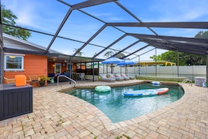 A swimming pool with lounge chairs and umbrellas, surrounded by a covered patio area. - Suncourt Retreat Sports Court Pool Hot Tub (Bradenton)