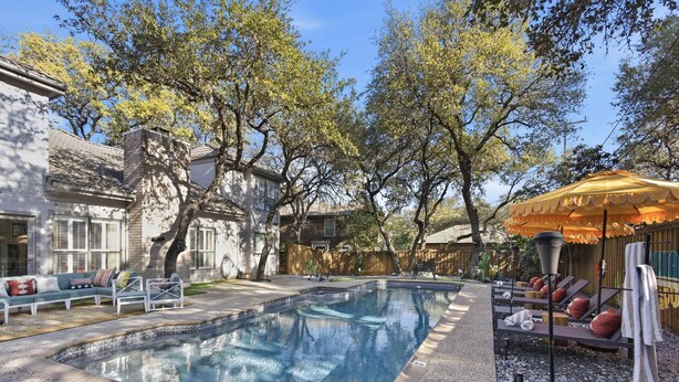 A swimming pool with lounge chairs and umbrellas, surrounded by trees and a building. - Ultimate Backyard Pool Game Room Kid s Room (San Antonio)