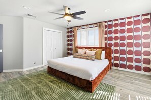 A bedroom with a bed, a ceiling fan, a window with curtains, and a patterned wall. - Ultimate Backyard Pool Game Room Kid s Room (San Antonio)