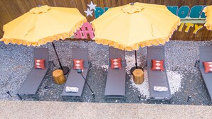 A row of sun loungers with yellow umbrellas, each with a wooden stump base, and red patterned pillows. - Ultimate Backyard Pool Game Room Kid s Room (San Antonio)