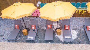 A row of sun loungers with yellow umbrellas, each with a wooden stump base, and red patterned pillows. - Ultimate Backyard Pool Game Room Kid s Room (San Antonio)